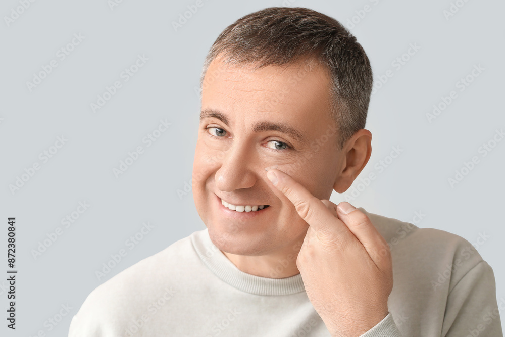 Wall mural Mature man putting in contact lenses on grey background