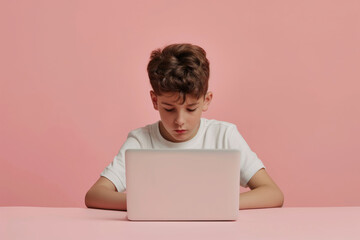 Young boy with brown hair focuses on laptop, studying online against a pink background, showcasing digital youth lifestyle