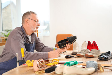 Male shoemaker with shoes writing on notebook in workshop