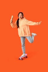 Young Asian woman with doner kebab and skateboard on orange background