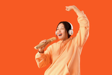 Young Asian woman in headphones with doner kebab singing on orange background