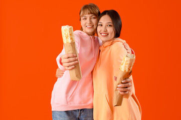 Young women with doner kebabs hugging on orange background