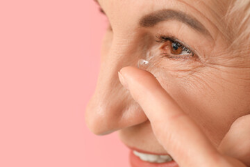Naklejka premium Mature woman putting in contact lenses on pink background, closeup