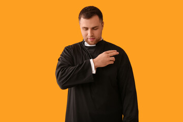Young priest cross oneself on yellow background