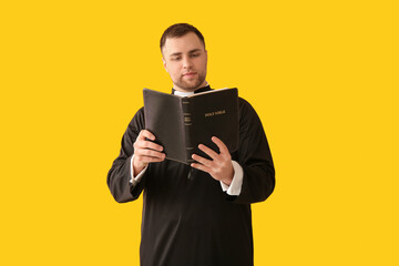 Young priest with Bible on yellow background