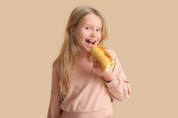 Cute little girl eating tasty hot dog on color background