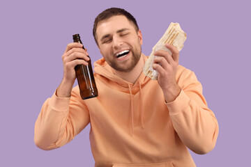 Handsome young man with tasty doner kebab and bottle of beer on lilac background