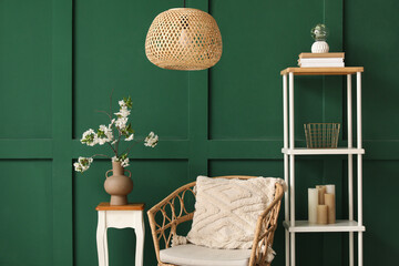 Vase with blooming branches on coffee table near cozy armchair in green living room