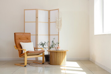 Interior of light living room with armchair, table and folding screen