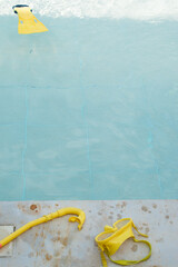 Vertical shot of yellow diving fins floating on blue pool water in sunny day, googles on pool edge