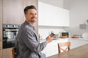 Young man using mobile phone with smart home security system control panel in kitchen