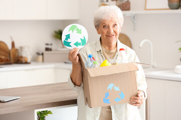 Senior woman with box of garbage and recycle sign in kitchen. Waste sorting concept