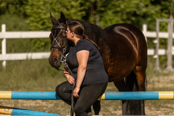 A female equestrian with her bay brown horse beneath a jumping obstacle during recovery of the horse