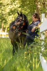 Portrait of a woman and her bay brown horse at a paddock in summer outdoors