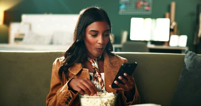 Popcorn, cellphone and woman relaxing on sofa watching funny video on social media or internet. Phone, smile and female person eating snack and reading comic blog on website in bedroom at apartment.