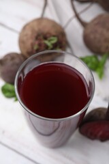 Fresh beet juice in glass and ripe vegetables on light wooden table, closeup