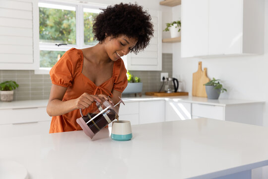 Pouring coffee from French press into cup, woman enjoying morning in kitchen, copy space