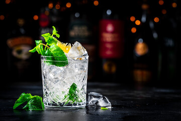 Summer refreshing drink cocktail with mint, lemon, vodka and gin tonic. Dark background bar counter