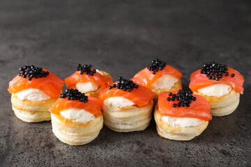 Delicious puff pastry with cream cheese, salmon and black caviar on grey table