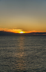 Fototapeta premium A small solitary fishing boat sails across the calm waters of the Skagerrak Sea, with the rising sun casting a golden glow on the horizon near the coast of Norway