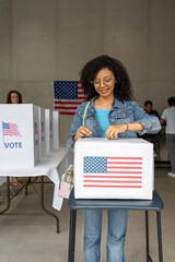 vertical portrait of a young african american woman voting in the us election, placing vote ballot in the polling box, vote in America. Concept of usa choice, democracy and freedom