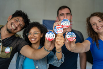 diverse group of smiling friends holding 2024 Vote election I voted buttons or pins at a US...