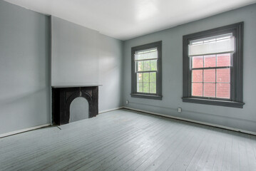 Historic Empty Room With Two Large Windows And A Black Fireplace, With Gray Walls And Floor