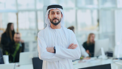 Professional Arab UAE Emirati man using smartphone on call. Happy Middle Eastern national wearing kandura at a business corporate location