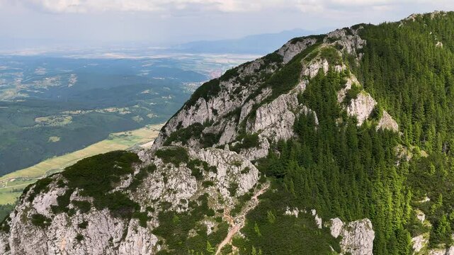 Drone flies right to left, revealing Zarnesti city against Piatra Mica peak on a sunny day