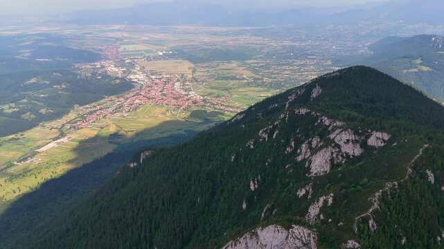 Drone pans left to right, revealing Zarnesti city and Piatra Mica peak