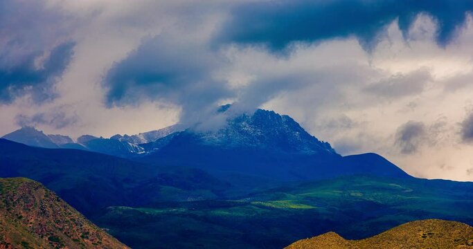clouds floating over snowcapped mountain peak at summer morning, telephoto timelapse