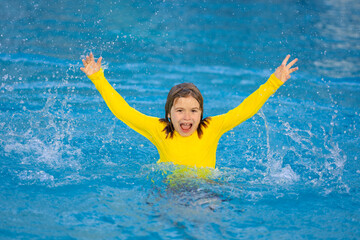 Excited child splashing water in pool. Little kid splashing in blue water of swimming pool. Cute boy swimming and splashing water with drops in pool. Child splashing and having fun in swim poolside.