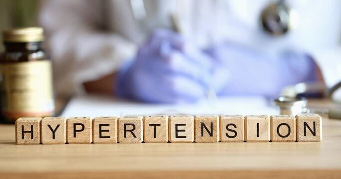 Doctor filling out medical documentation against background of wooden cubes with word hypertension closeup 4k movie. Diagnosis and treatment of arterial hypertension concept
