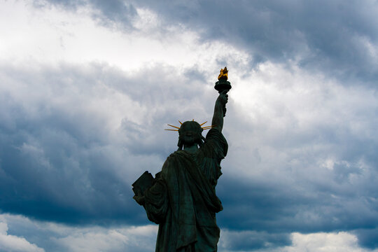 Statue de la liberté vue de derrière à contrejour (silhouette), face à un ciel de nuages d'orage. Concepts de menace et de danger pour la liberté et pour la démocratie