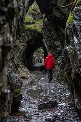 Obraz premium Visualize a solitary figure wearing a red jacket, walking through a tunnel carved in rock, evoking a sense of exploration and adventure in a natural environment.