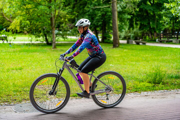 Cycling training in city. Young joyful woman in white helmet and colorful blouse and black shorts...