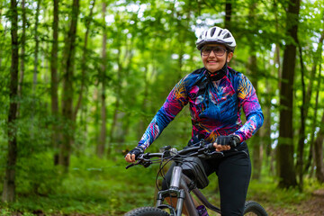 Obraz premium Cycling training in city. Young joyful woman in white helmet and colorful blouse and black shorts riding bike on bike path in city. Playing sports outdoors in spring. Healthy lifestyle