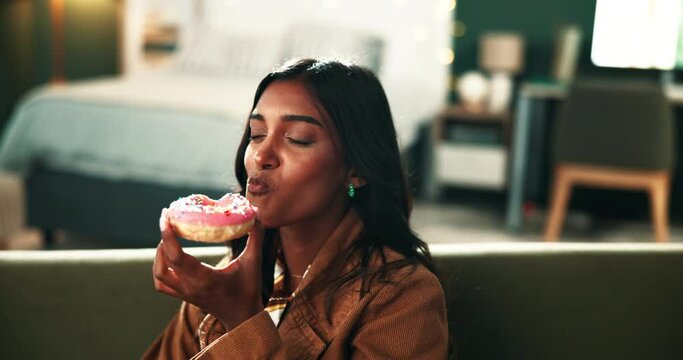 Woman, donut and relax with eating on sofa with fast food, sweets or sprinkles with memory in apartment. Person, hungry and house with cake, dessert and pastry on couch in home with craving in Mumbai