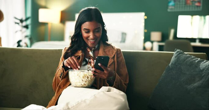 Popcorn, phone and woman relaxing on sofa watching funny video on social media or internet. Cellphone, smile and female person eating snack and reading comic blog on website in bedroom at apartment.