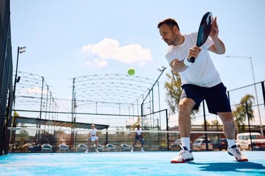 Male athlete playing paddle tennis on outdoor court.