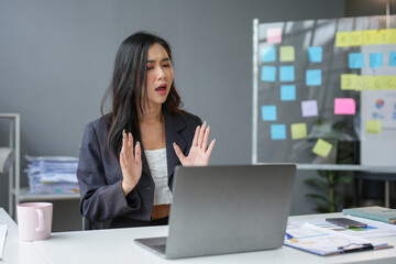 Asian businesswoman sitting and working with laptop computer Use the phone to talk via video call. online in financial business Business ideas to start online through the media.