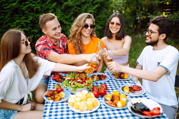 Group of friends having backyard dinner party together. Young people enjoying leisure time together outside toasting with beer and barbecue. Vacation, picnic, weekend, nature.