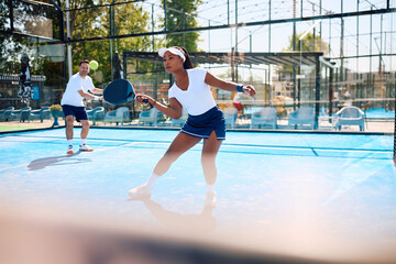 Black athletic woman playing paddle in mixed doubles on outdoor court.