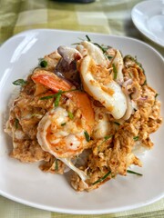 Omelette with shrimp and seafood on rice and sauce on white ceramic plate and spoon and fork.