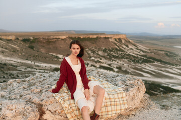 Woman enjoying nature relaxing on top of a rock with plaid blanket in travel destination beauty