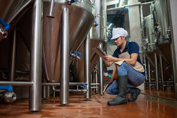 Fototapeta premium Asian man works at a craft beer factory as a brewer operating the brewery machinery. Craft beer production is a small business.