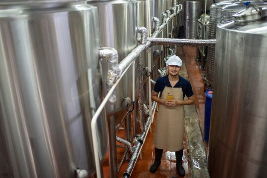 An Asian male brewer tests beer samples by pouring beer - Powered by Adobe