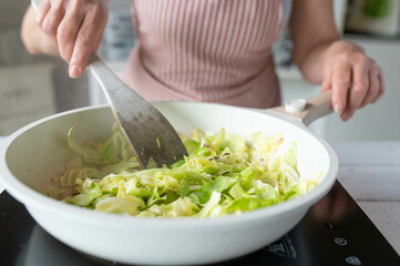 Woman frying cabbage in a frying pan in the kitchen. Homemade cooking