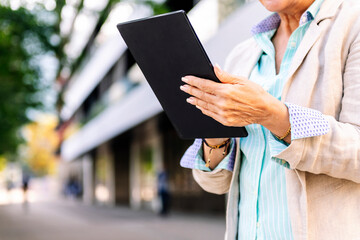 unrecognizable mature woman using digital tablet outdoors in the city, concept of urban lifestyle in adulthood and technology o communication, copyspace for text