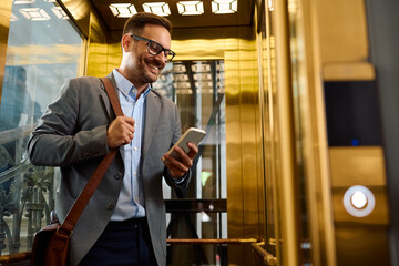 Happy businessman using cell phone in  elevator.